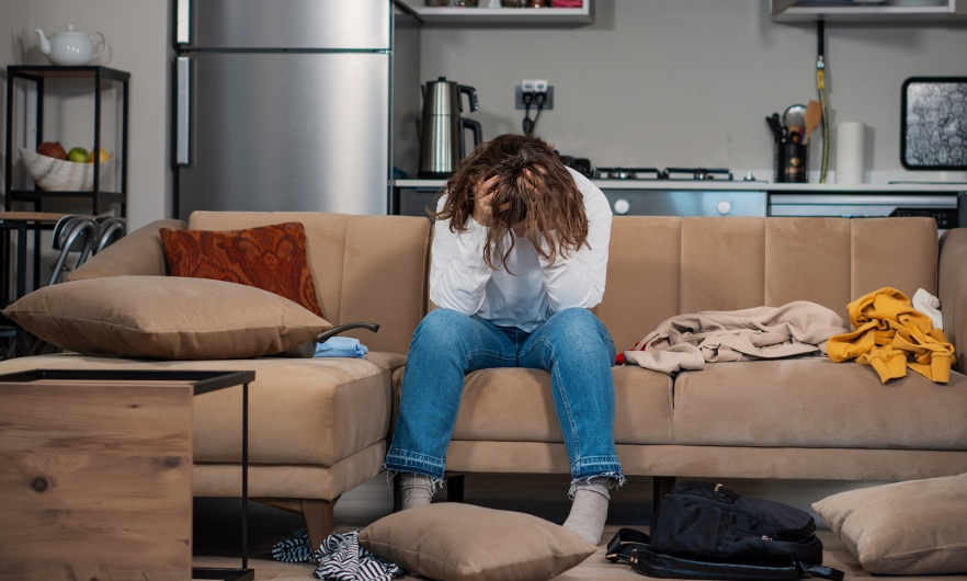 Person sitting on the couch looking frustrated with their head down and hands through their hair.
